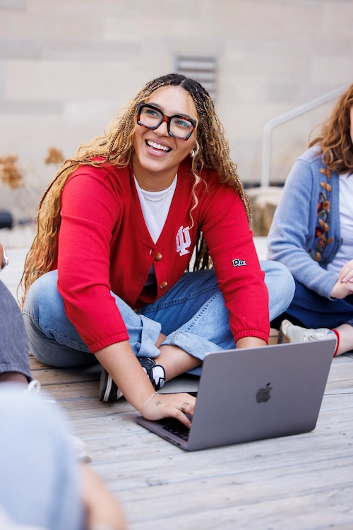 Student sitting outside smiling and using a laptop.